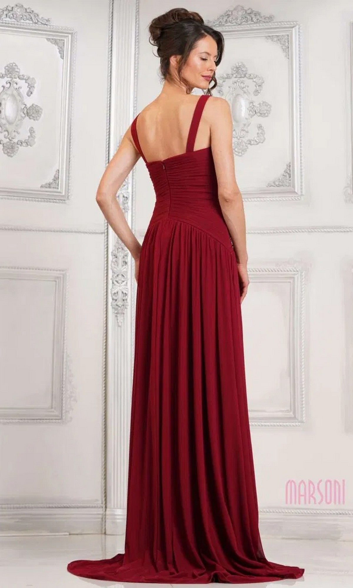 A woman in the Marsoni MV1316 long burgundy formal dress with a ruched bodice stands facing away in an ornate, white-paneled room.